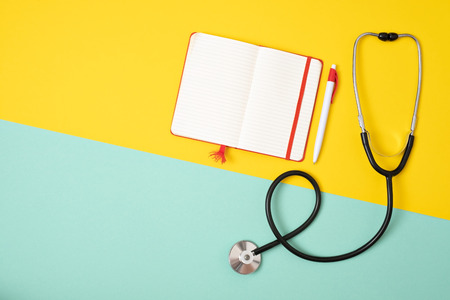 Medical phonendoscope or stethoscope with empty notebook isolated on yellow and blue background with copyspace. Top flat lay view. Make a diagnosisの写真素材