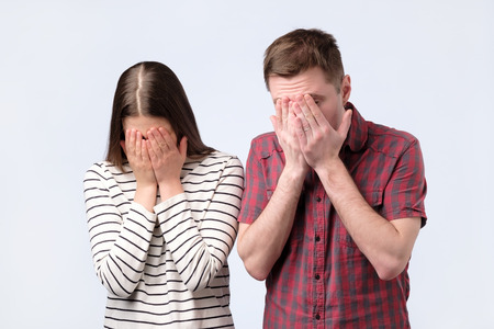 Portrait of a young european couple covering face with hands