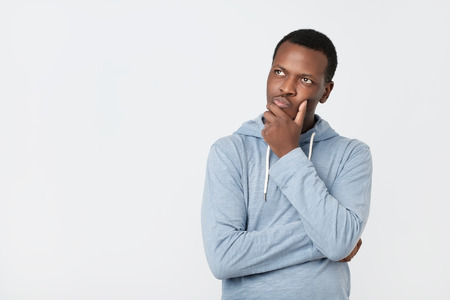 Handsome young African American man looking up with thoughtful and skeptical expression, trying to remember something