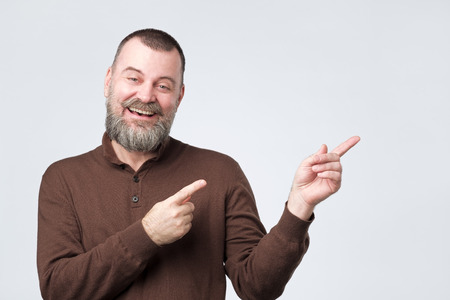 Laughing mature man with beard pointing finger asideの写真素材