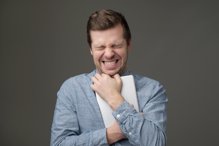shocked man hugs a tablet on a gray backgroundの写真素材