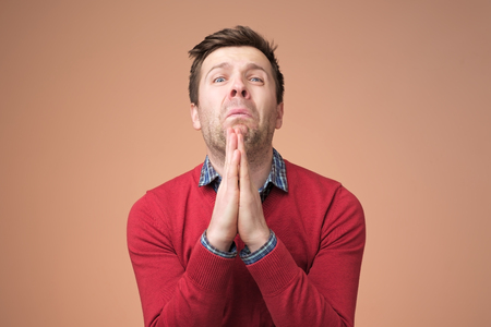 Desperate young man showing clasped hands, sorry for mistakeの写真素材