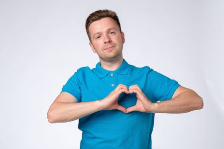 Handsome man in blue shirt making a heart with his handsの写真素材