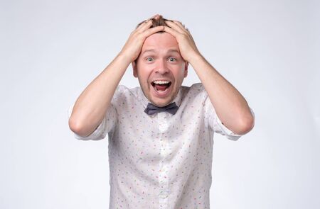 Excited casual man standing with raised hands near faceの写真素材