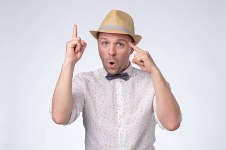 Tourist man in summer hat has excited expression, index finger up, recieve good idea