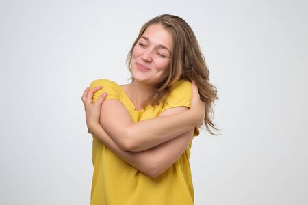 Positive relaxed young woman closing eyes with pleasure, keeping arms around herself. Selfish and egoist person concept.の写真素材