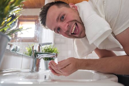 Caucasian man washing face in a wash basin in white washroomの写真素材