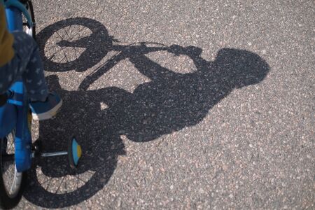 Shadow of kid riding bicycle on ground.