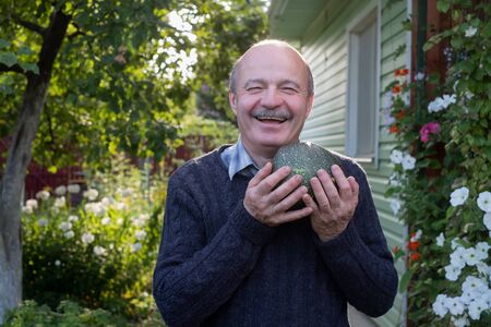 Senior hispanic man holding fresh seasonal green zucchini smiling being content
