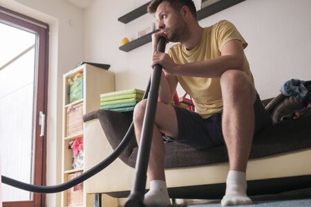 man sitting tired after cleaning floor with vacuum cleanerの写真素材
