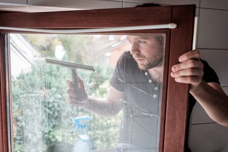 man washes a window in a house using scraper