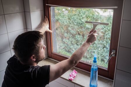 Caucasian man washes a window in a house using scraperの写真素材