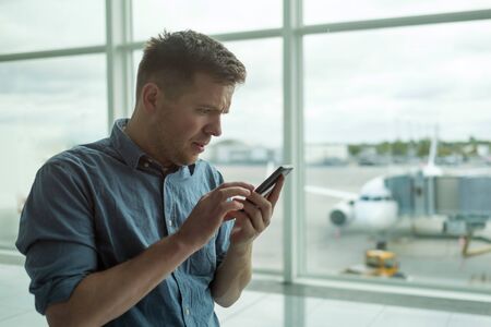 man in anxious looks at the phone standing near window at the airportの写真素材
