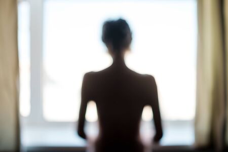 Unknown female person standing near window alone. Negative facial human emotionの写真素材