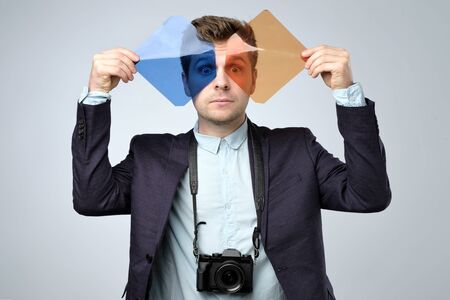 Young man photographer with dslr camera holding color filtersの写真素材
