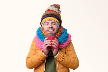 Handsome man in several winter hat and scarf drinking coffee.