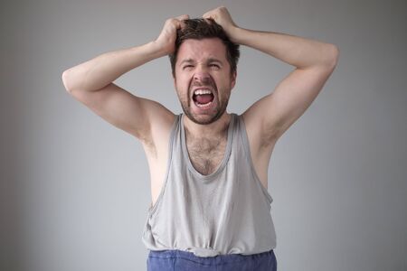Untidy young man screaming and pulling his hair.