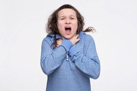 Pretty caucasian female teenager in blue clothes feeling storng pain in throat choking herself ith...