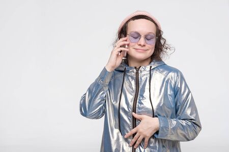 Cute pretty woman in glasses and pink hat talking to her friend with phone. Studio shot