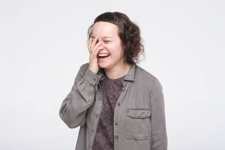 Pretty caucasian young woman being shy laughing covering her mouth with hand. Studio shot. Posititve...