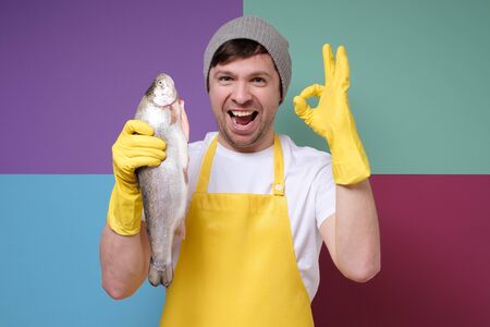 fisher with yellow apron holding a big salmon, trout fish showing ok signの写真素材