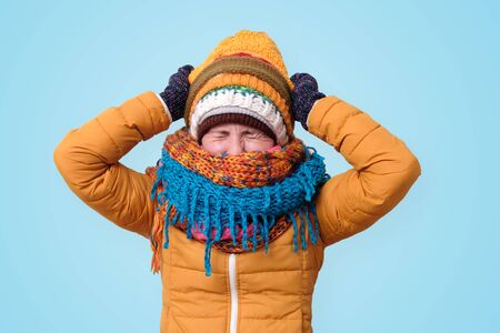 Girl dressed in warm clothes, hats and scarfs holding hands on head in despair and frustration.の写真素材