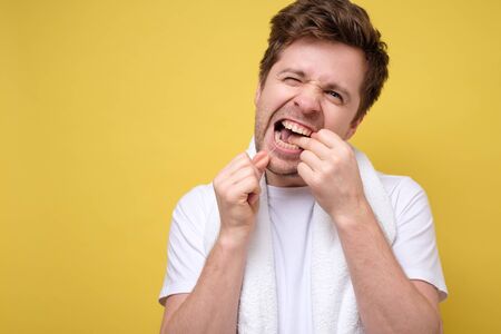 Young caucasian man in white shirt hold using dental floss isolated on yellow wall background