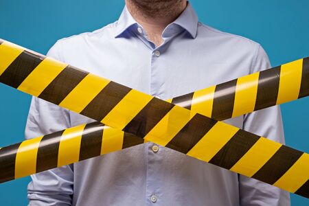 Man standing behind black and yellow lines of barrier tape that forbids passage. Concept of No entry. Protection from coronavirus.の写真素材