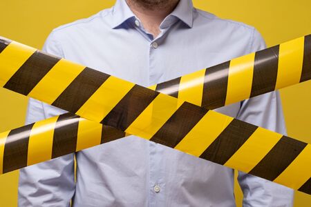 Man standing behind black and yellow lines of barrier tape that forbids passage. Concept of No...