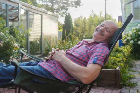 Adult man in casual clothing sitting in a deck chair and resting having a nap.