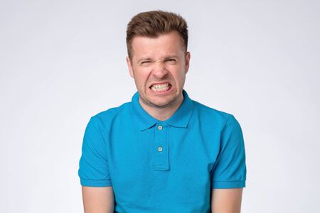Young angry man is about to lose his temper on gray background. Negative facial human emotion.