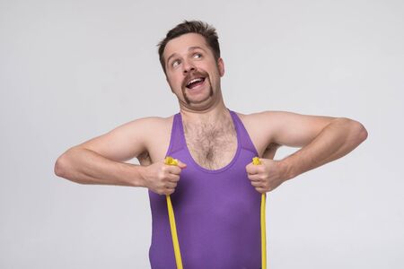 Young caucasian man exercising with rubber tapes isolated on grey wall.