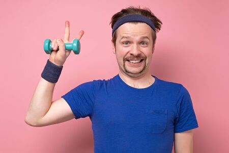 Young sporty caucasian man showing number two with fingers or victory gesture. Studio shot on pink...