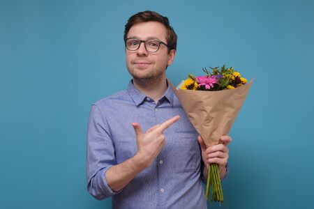 Young caucasian man in pink t-shirt holding flowers as gift for his mother or girlfriendの写真素材