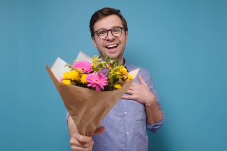 Young caucasian man in pink t-shirt holding flowers as gift for his mother or girlfriendの写真素材