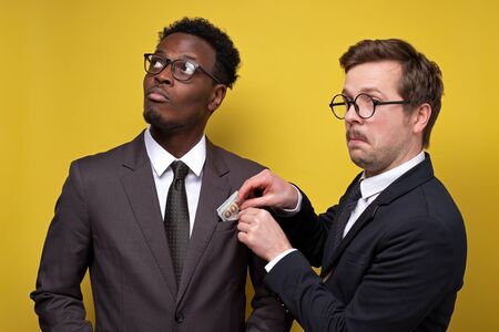 Young man in suit giving bribe to business partner on yellow backgroundの写真素材