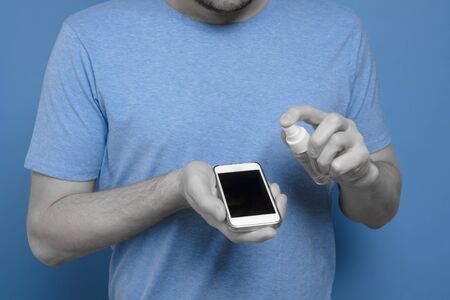 Caucasian man disinfecting his smartphone by spraying a sanitizer from a bottle.