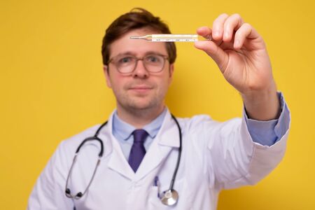 doctor holding a medical thermometer smiling. His patient is recovered.
