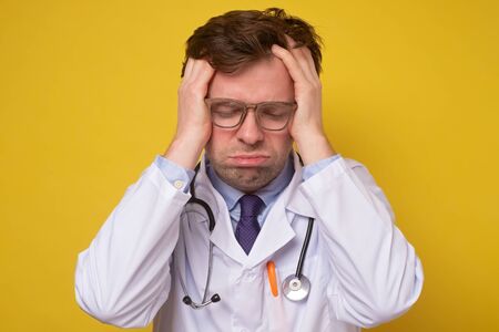 Tired man doctor in eyewear massaging temples, suffering from sudden headache.