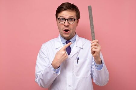 Young caucasian male doctor holding a measuring metal ruler with shocked faceの写真素材
