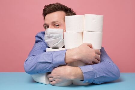 Excited caucasian man in medical mask is happy ge have a stock of toilet paper. Studio shotの写真素材