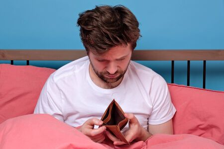 Unemployed sad caucasian man sitting at home showing empty wallet