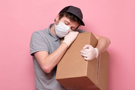delivery man in medical mask holding a cardbox being exhausted with overtime workの写真素材