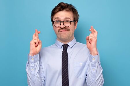 Young caucasian businessman in funny glasses making a wish isolated on blue background.の写真素材