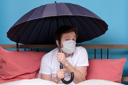 Man in medical mask holding an umbrella sitting at the bedの写真素材