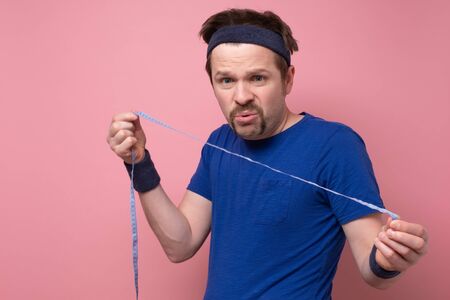 Man taking measurements of his body by centimeter line. He looks amazed as does not see results of...