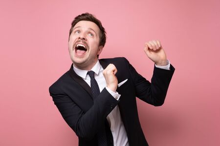 Caucasian young businessman with mustache wearing suit dancing and singing on pink wall. Celebration og success. Studio shotの写真素材