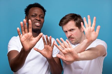 Two men african american and caucasian making stop sign making a social distance or refusing...