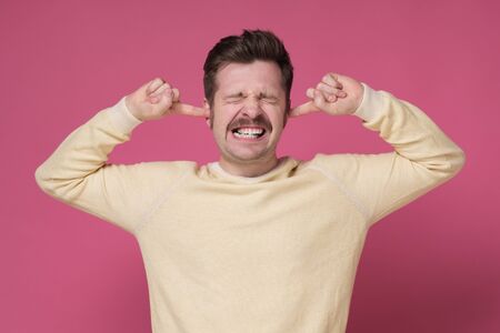 Stop that loud noise concept. Mature man in yellow sweater suffering from loud music and pain trying to plug ears.の写真素材