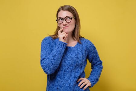 Caucasian young woman holding hand near chin trying to make a right decisionの写真素材
